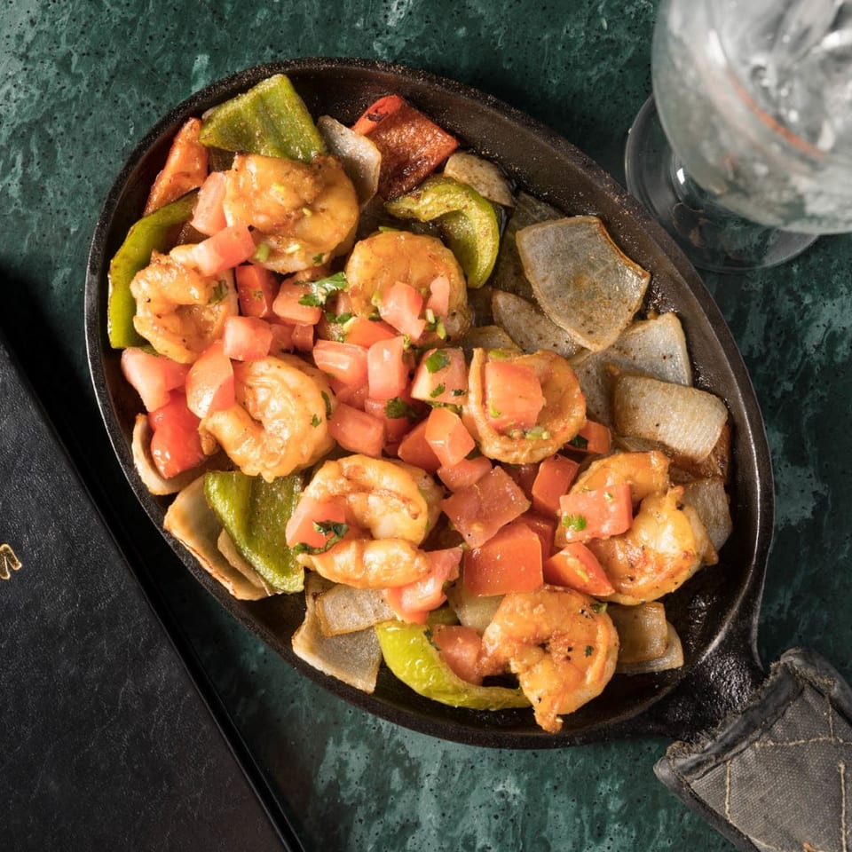 Sizzling shrimp fajitas with bell peppers, onions, and diced tomatoes in a cast iron skillet.