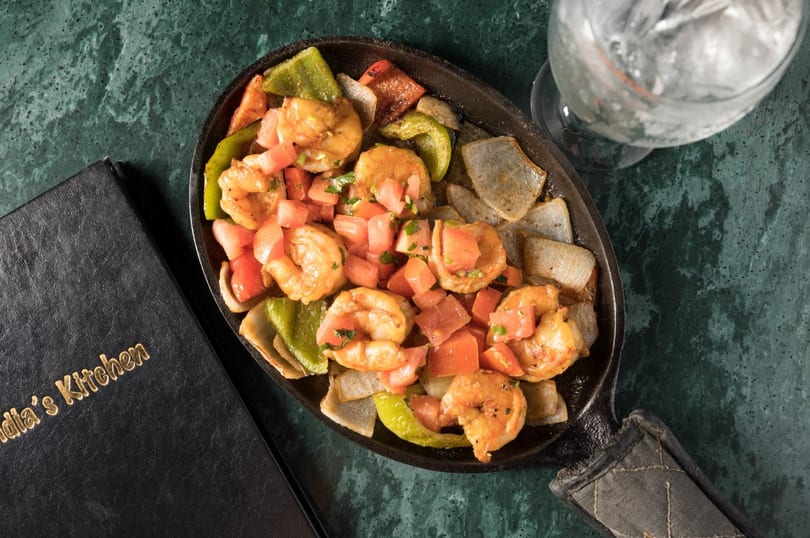Sizzling shrimp fajitas with bell peppers, onions, and diced tomatoes in a cast iron skillet.