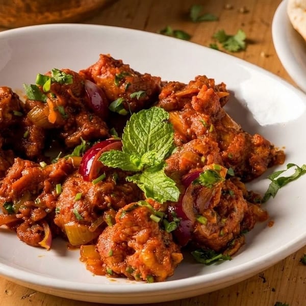 Spicy chicken Manchurian with red onions, green herbs, and mint on a white plate.