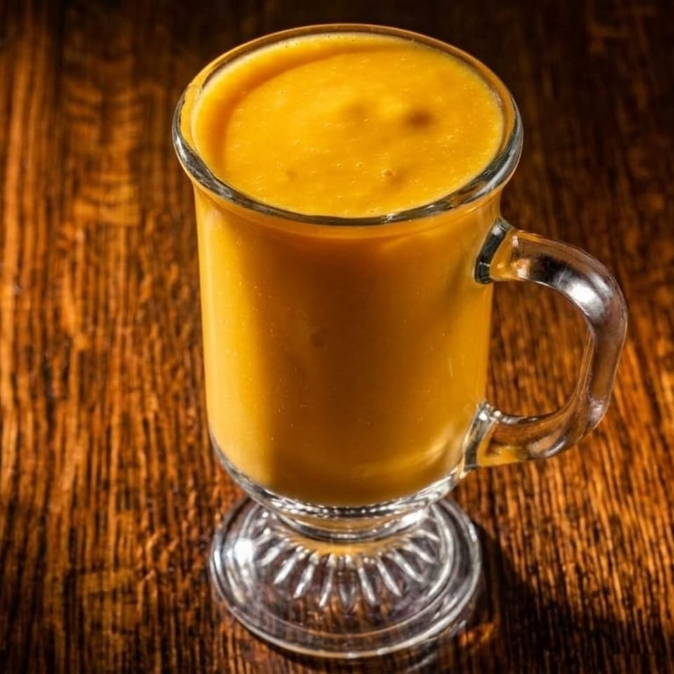 A tall glass mug filled with a vibrant orange smoothie sits on a dark wooden table.