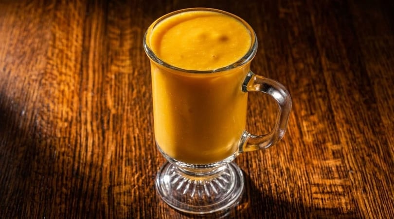 A tall glass mug filled with a vibrant orange smoothie sits on a dark wooden table.