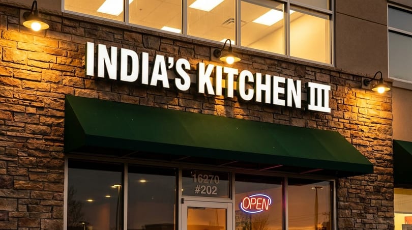 Exterior of India's Kitchen III restaurant with a green awning, stone facade, and an "OPEN" sign.