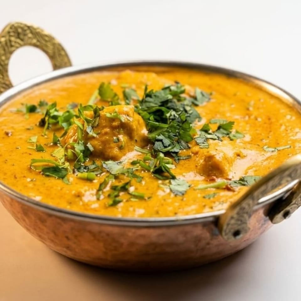 A copper karahi bowl filled with creamy orange butter chicken, garnished with fresh cilantro.