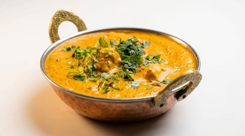 A copper karahi bowl filled with creamy orange butter chicken, garnished with fresh cilantro.