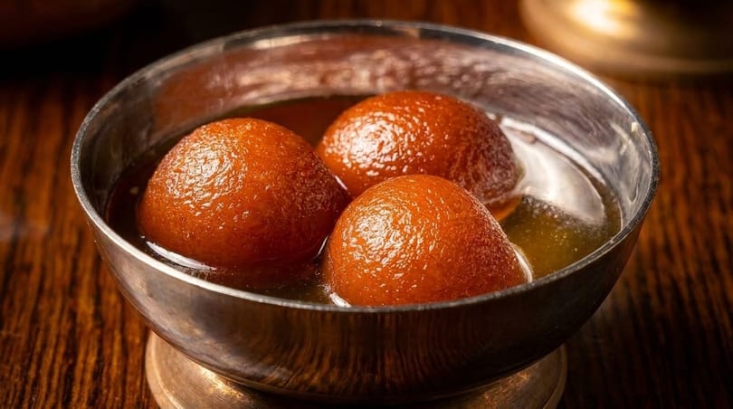 Three gulab jamun, Indian fried dough balls, soaked in syrup in a silver bowl.