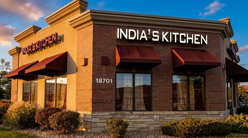 Exterior of India's Kitchen restaurant with brick facade, red awnings, and prominent signage at sunset.
