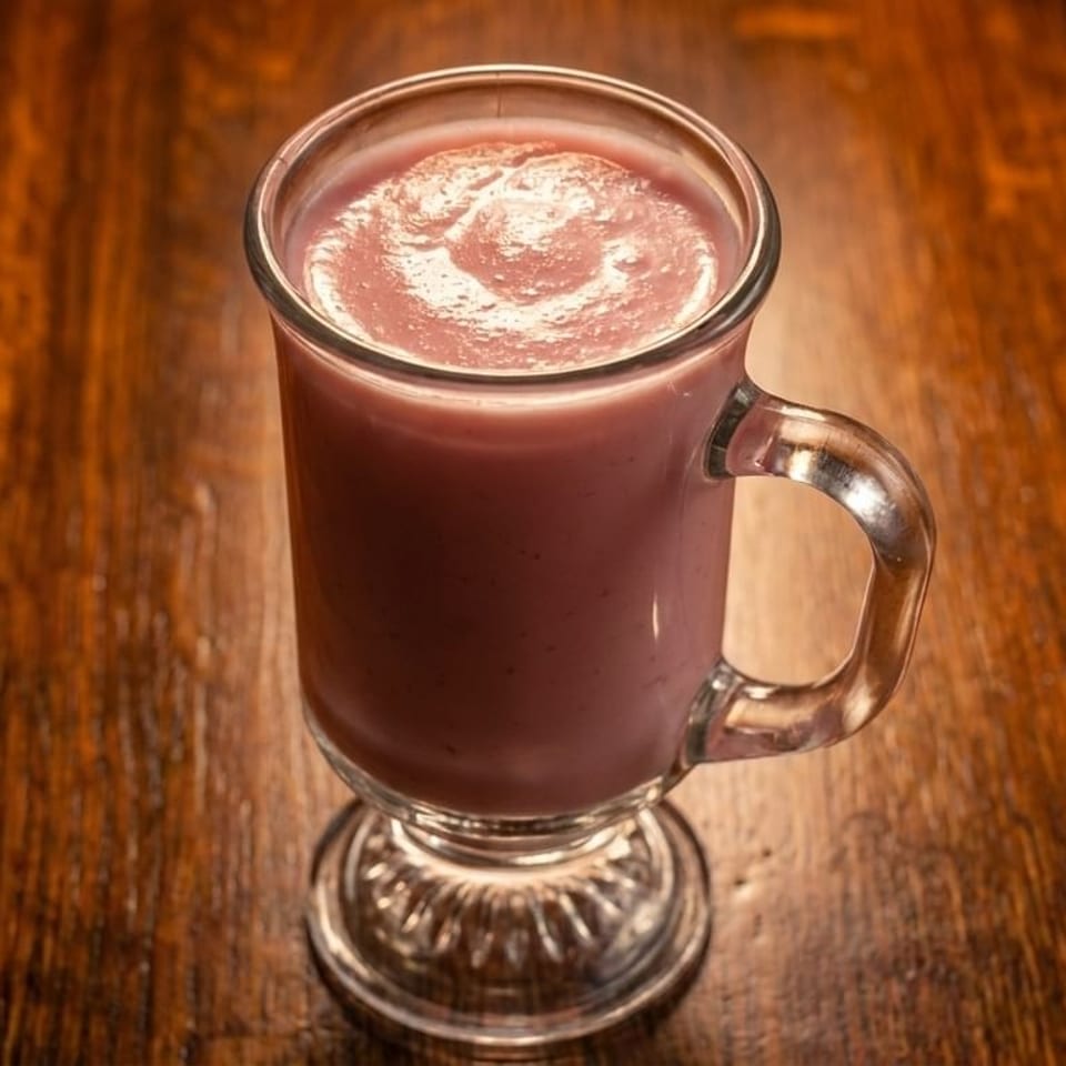 Pink smoothie in a clear glass mug with a handle, sitting on a dark wooden table.