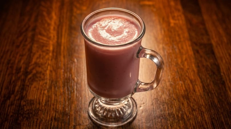 Pink smoothie in a clear glass mug with a handle, sitting on a dark wooden table.