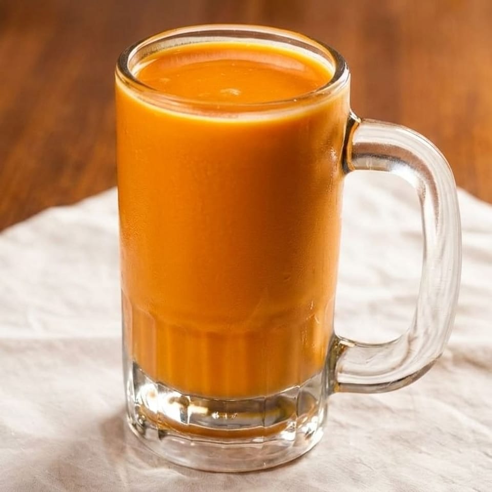 A glass mug filled with a vibrant orange beverage, possibly Thai iced tea, on a white napkin.