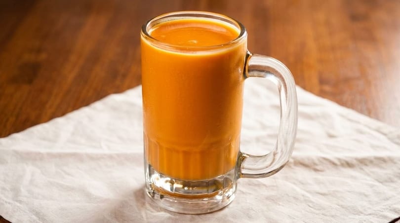 A glass mug filled with a vibrant orange beverage, possibly Thai iced tea, on a white napkin.